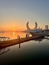 Sunrise at Lusail Marina in Qatar, featuring a serene waterfront view with yachts docked and the iconic Katara Towers reflecting on the water. A perfect blend of luxury and natural beauty.